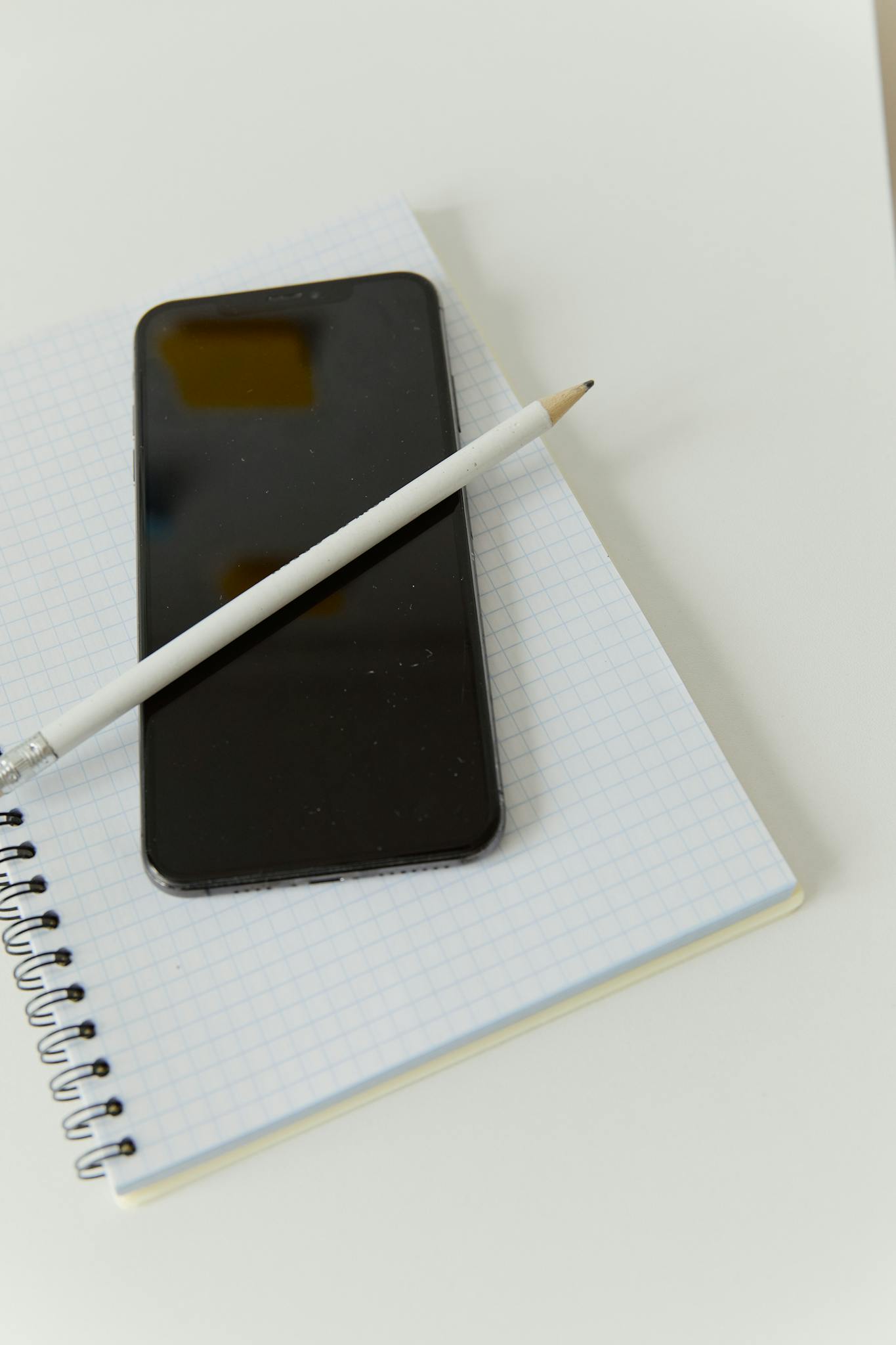 Close-up of a smartphone resting on a grid notebook with a pencil on top.
