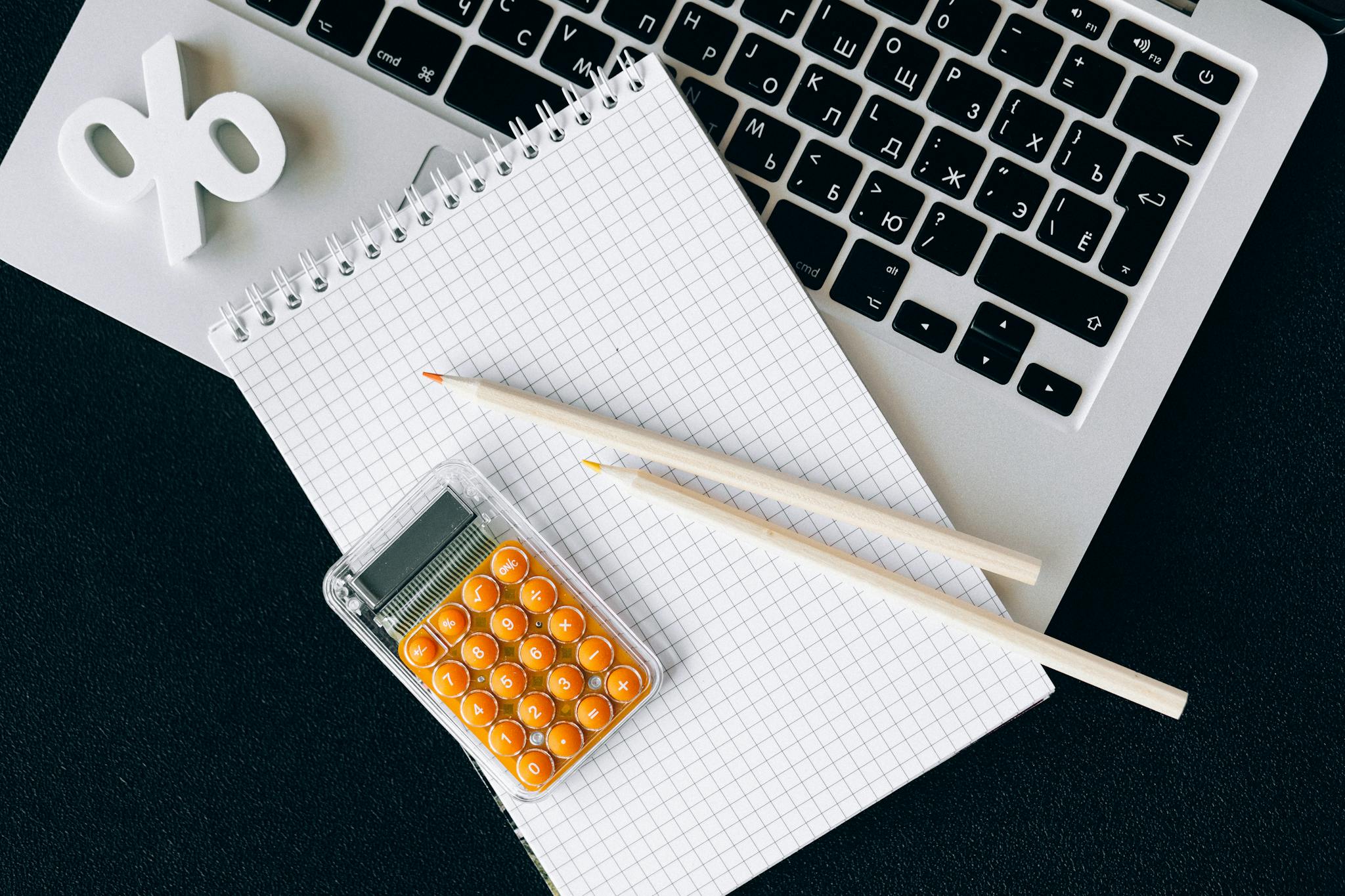 Flat lay of office supplies including a calculator and notebook on a laptop desk.